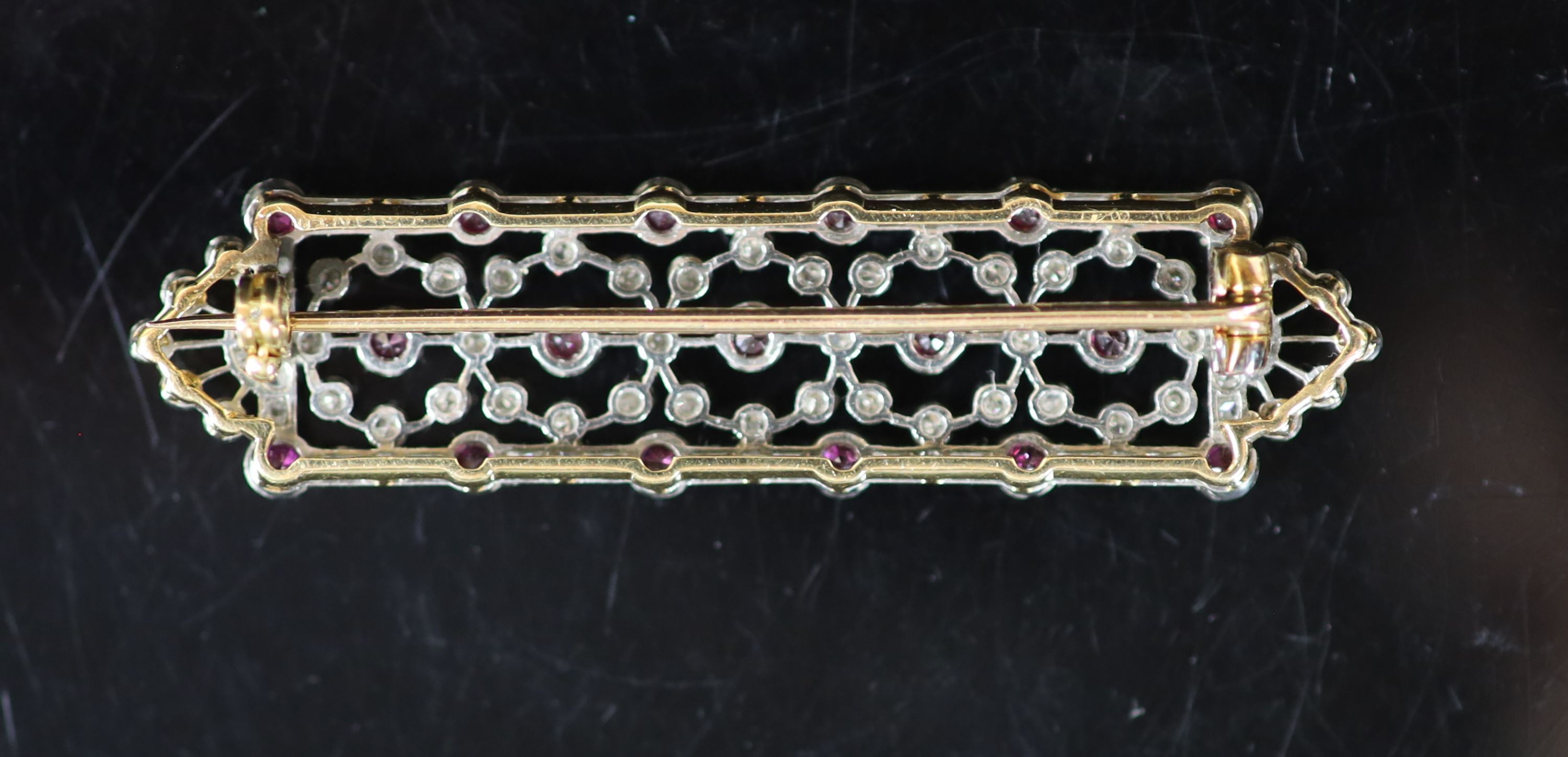 A 1920's/1930's style pierced gold and platinum, ruby and diamond chip millegrain set shaped oblong cluster brooch